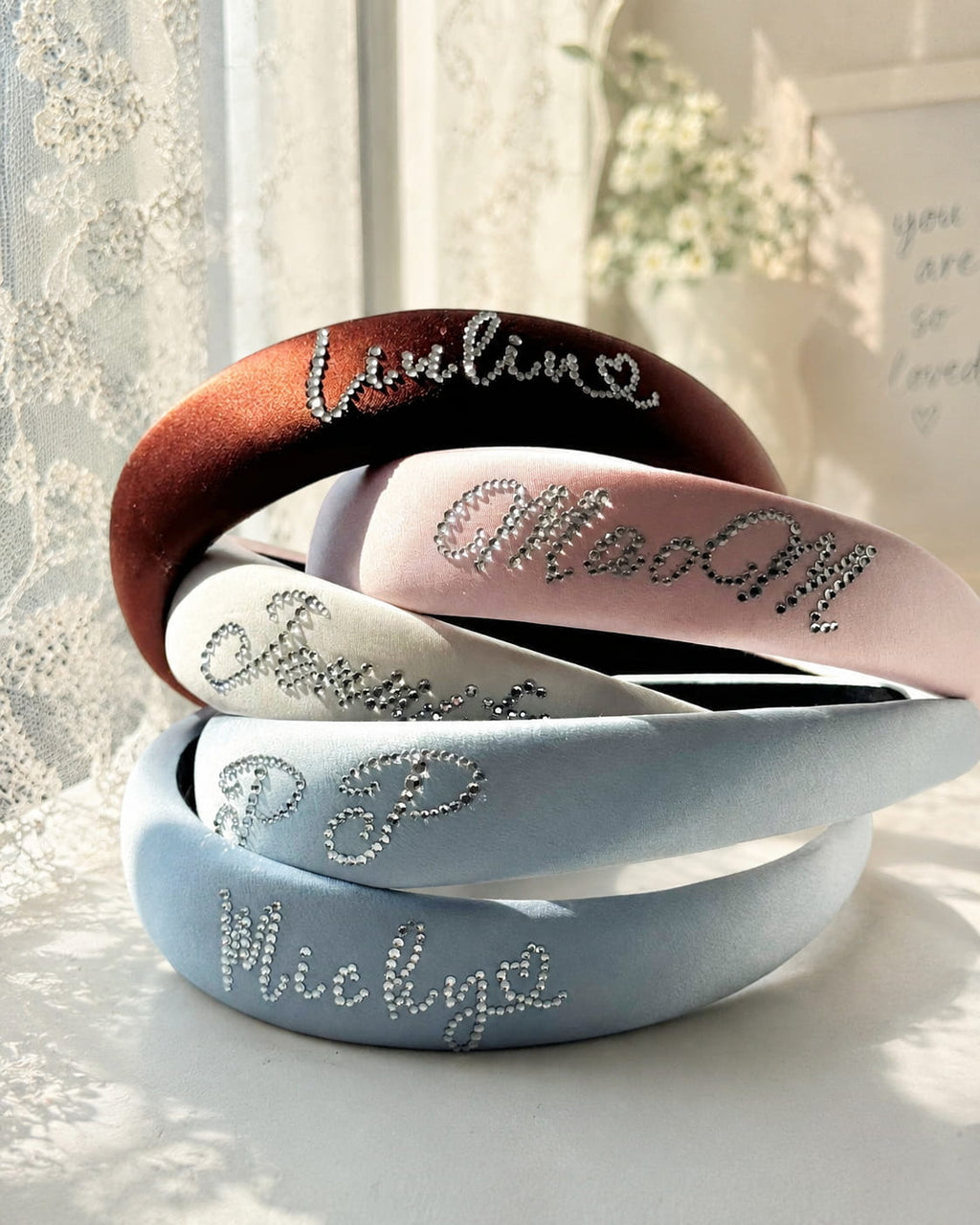 Custom silk padded headbands with rhinestone name lettering in soft natural sunlight.