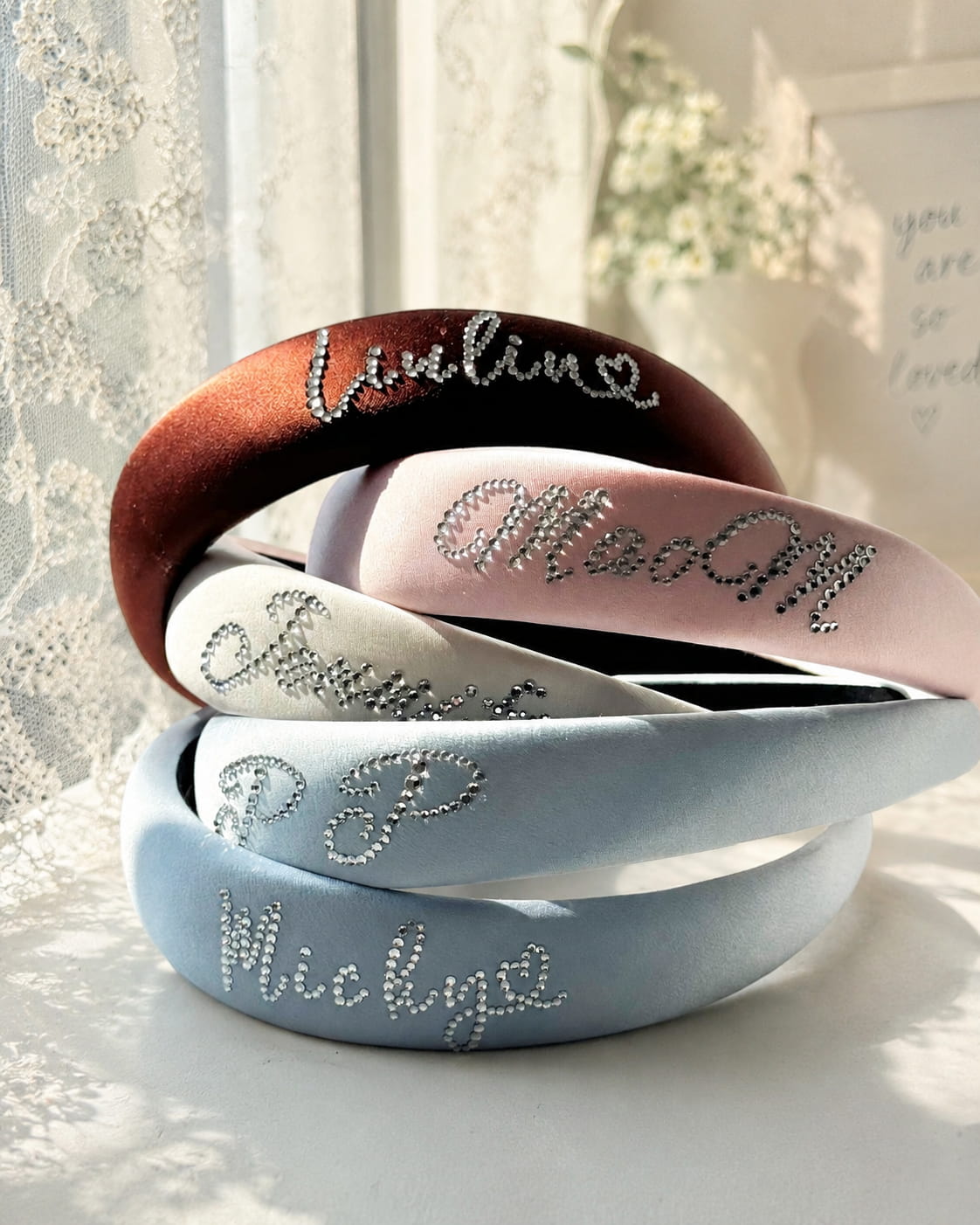 Custom silk padded headbands with rhinestone name lettering in soft natural sunlight.