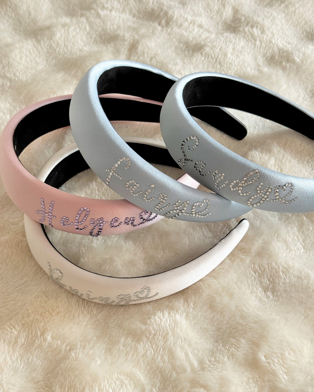 Personalized silk padded headbands in pink, blue, and ivory with rhinestone name lettering.