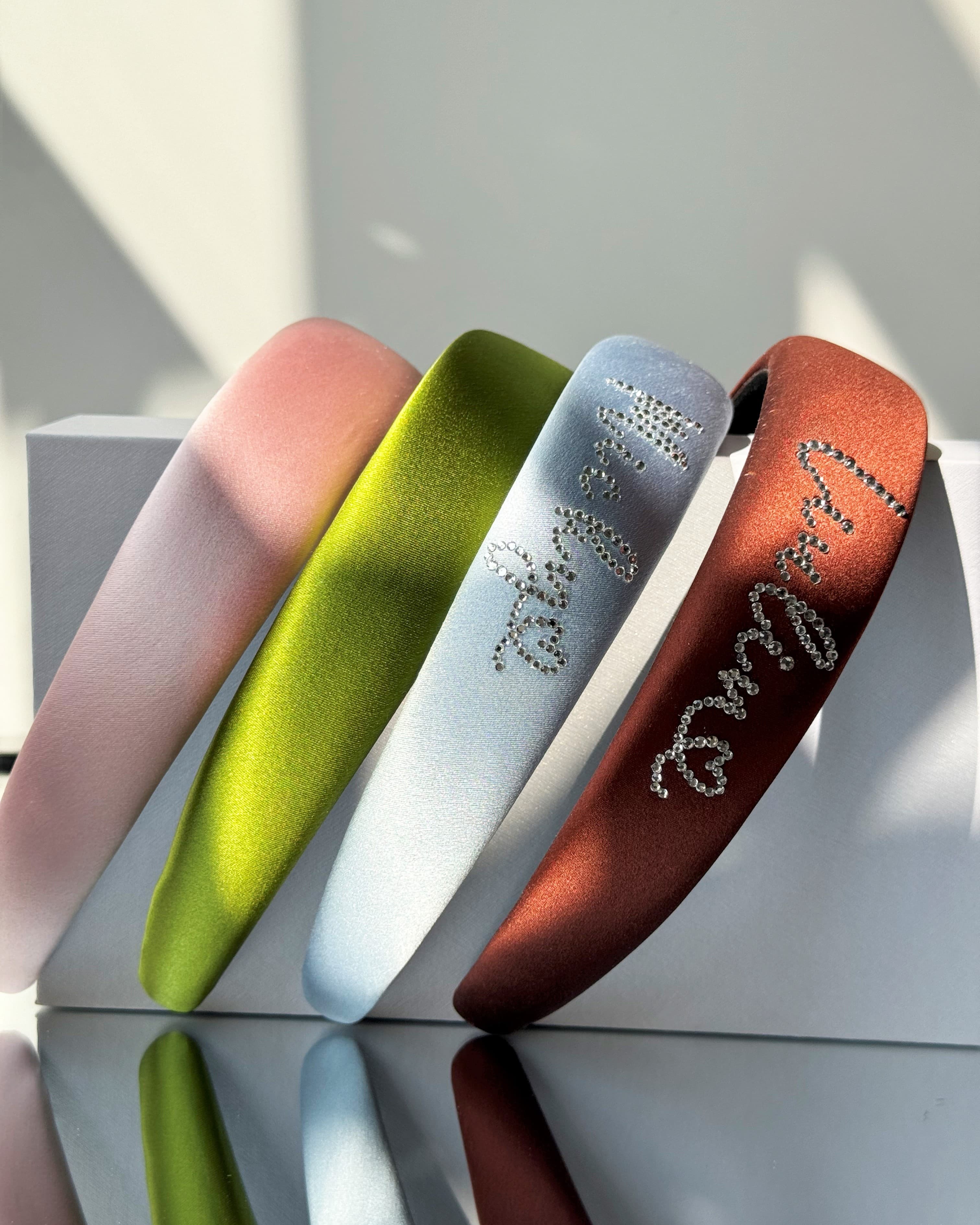 Personalized silk padded headbands in pink, green, blue, and brown with rhinestone lettering.