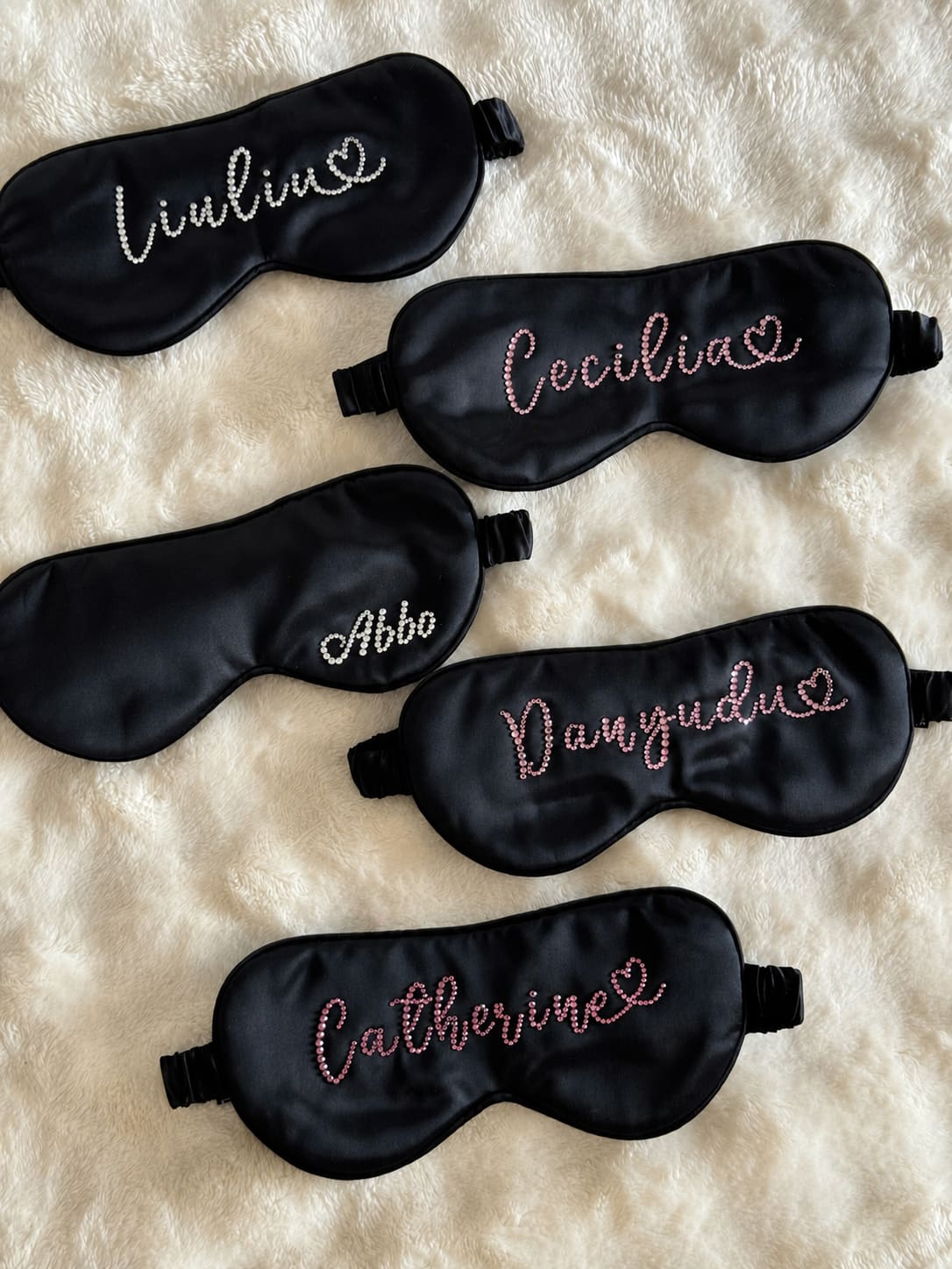 Black 22 momme silk sleep masks with custom rhinestone names displayed on a soft plush background.