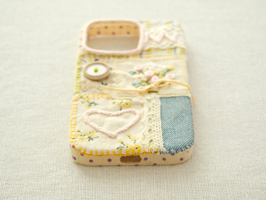 Bottom view of the "Floral Heart" patchwork case with a charging port cutout and yellow hand-stitched border.