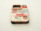 Bottom view of the cherry patchwork case with a charging port cutout and a red hand-stitched blanket stitch border.