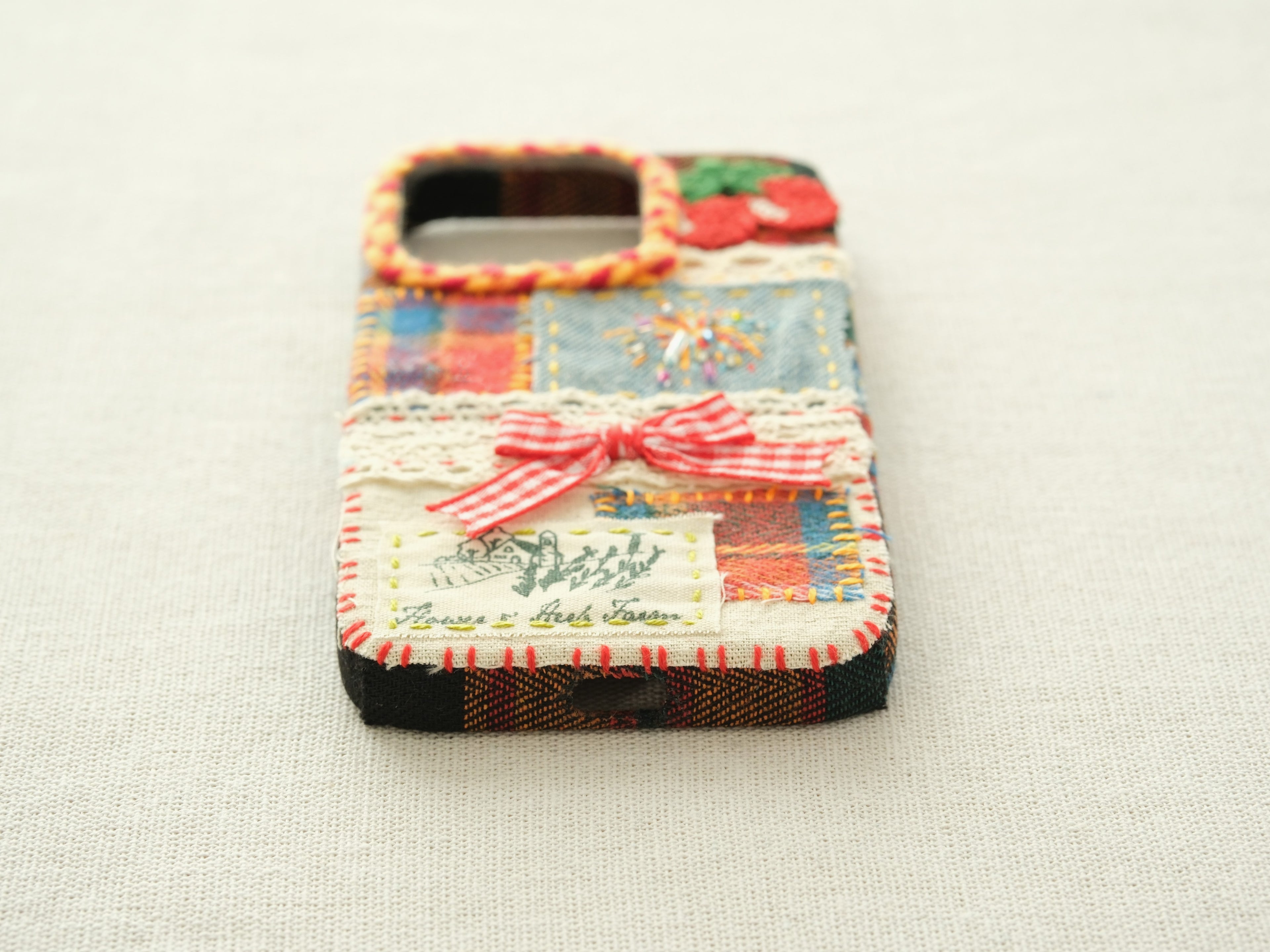 Bottom view of the cherry patchwork case with a charging port cutout and a red hand-stitched blanket stitch border.