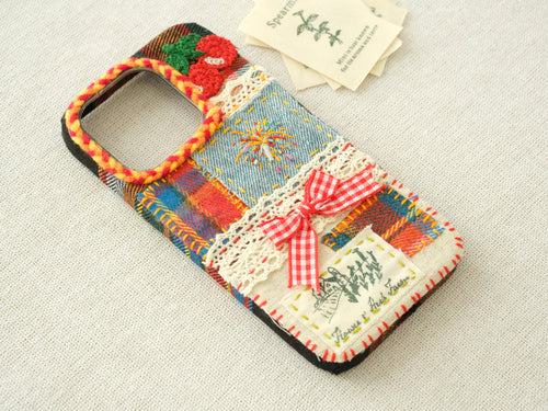 Side view of the patchwork case featuring 3D cherries, a red bow, and a hand-braided camera border.