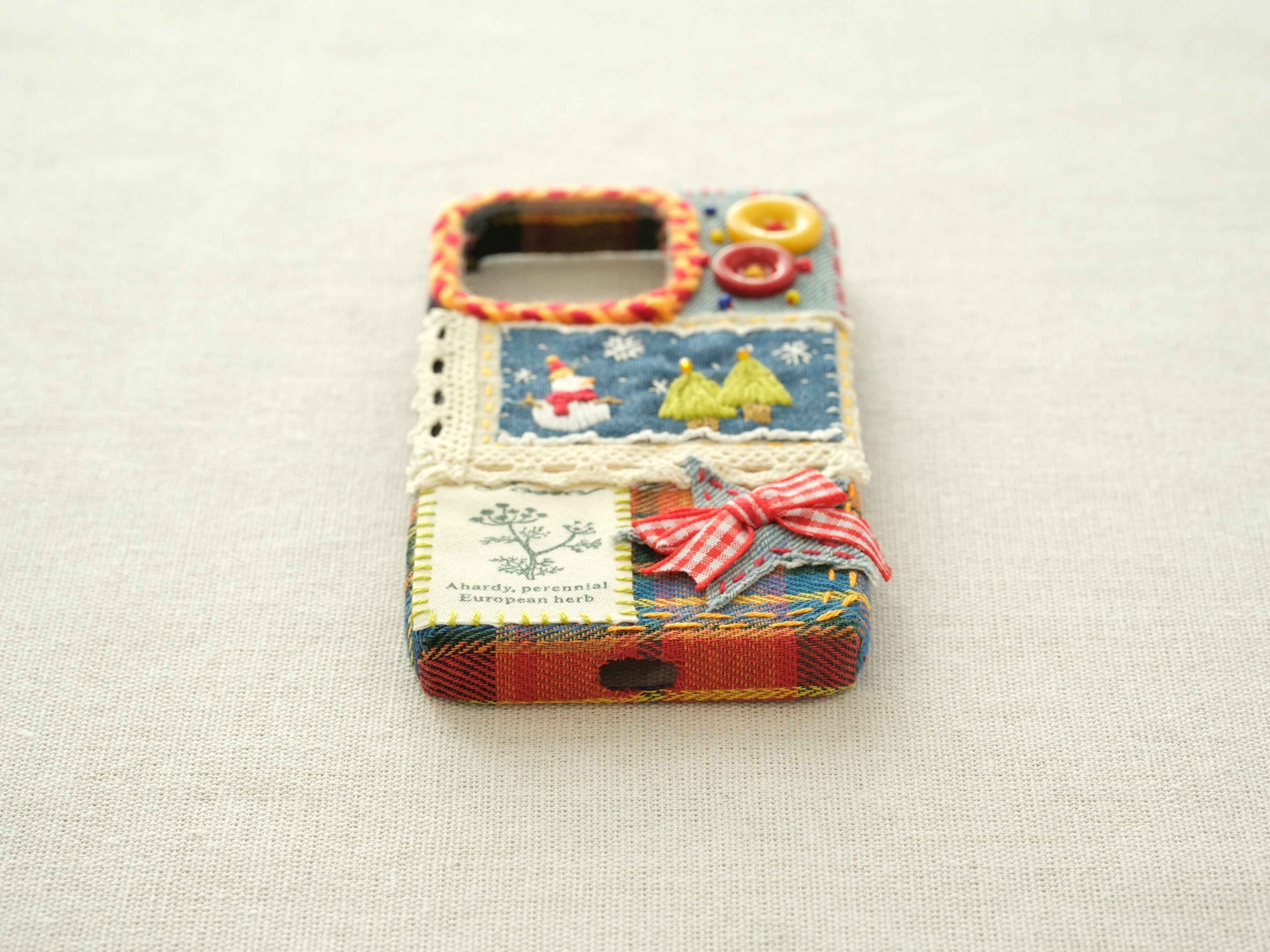 Bottom view of the snowman patchwork case with a charging port cutout and a yellow hand-stitched blanket stitch border.