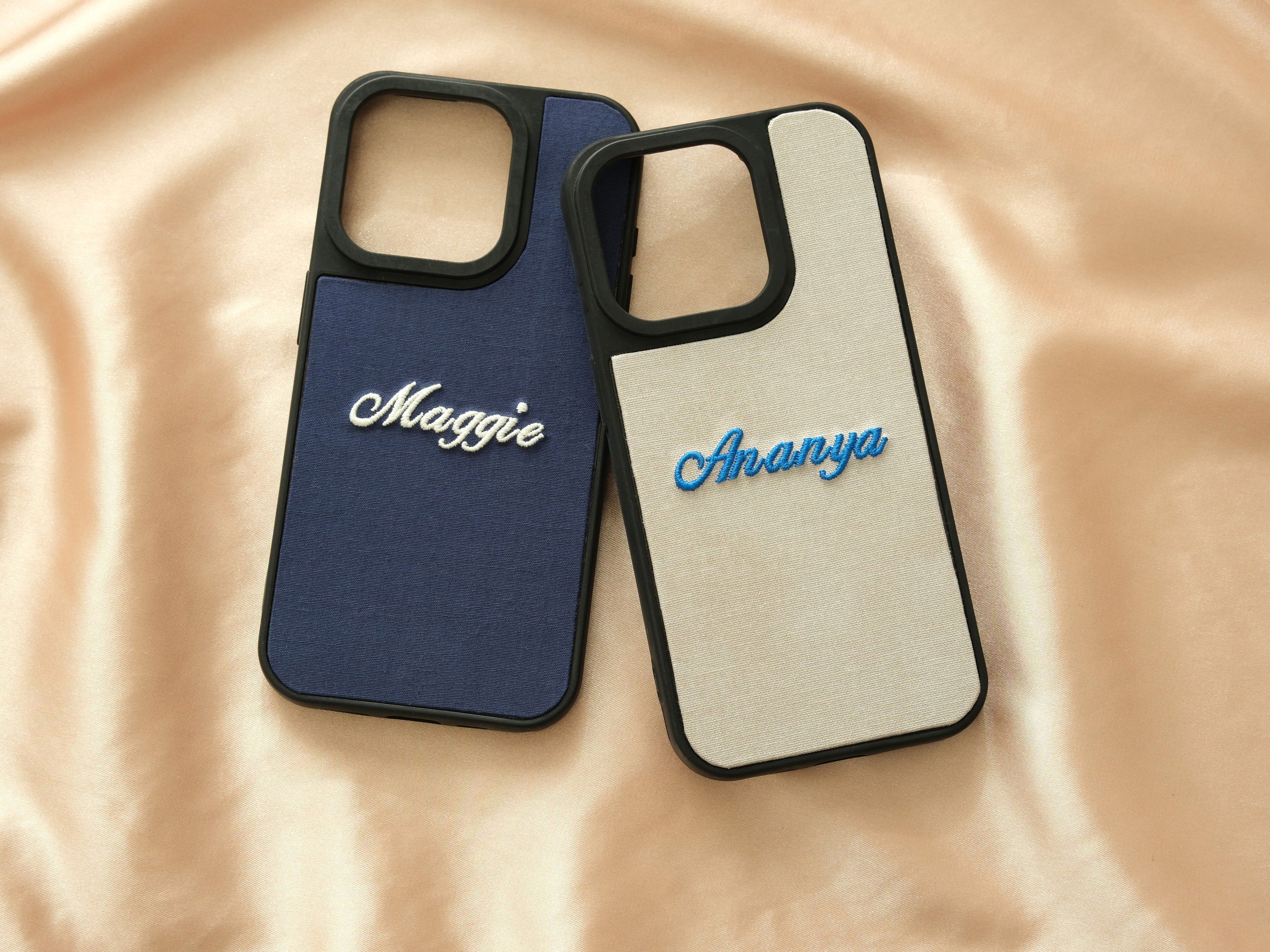 Two personalized fabric phone cases with embroidered names "Maggie" and "Ananya" on blue and cream backgrounds.