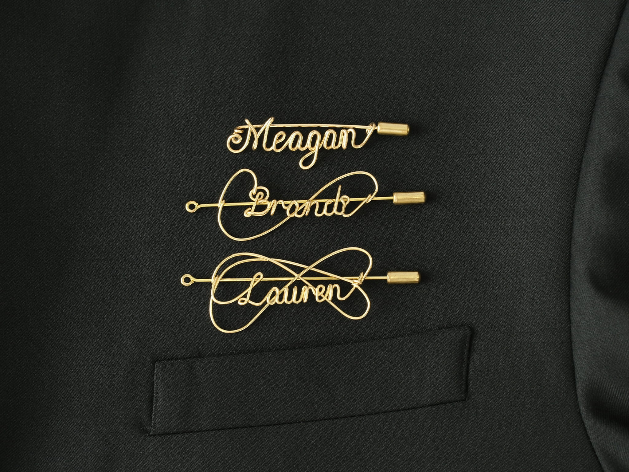 Custom name brooch in gold-plated copper wire on a black jacket, handcrafted jewelry.