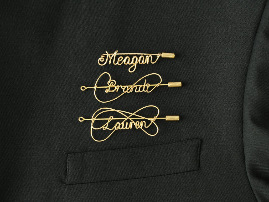 Custom name brooch in gold-plated copper wire on a black jacket, handcrafted jewelry.