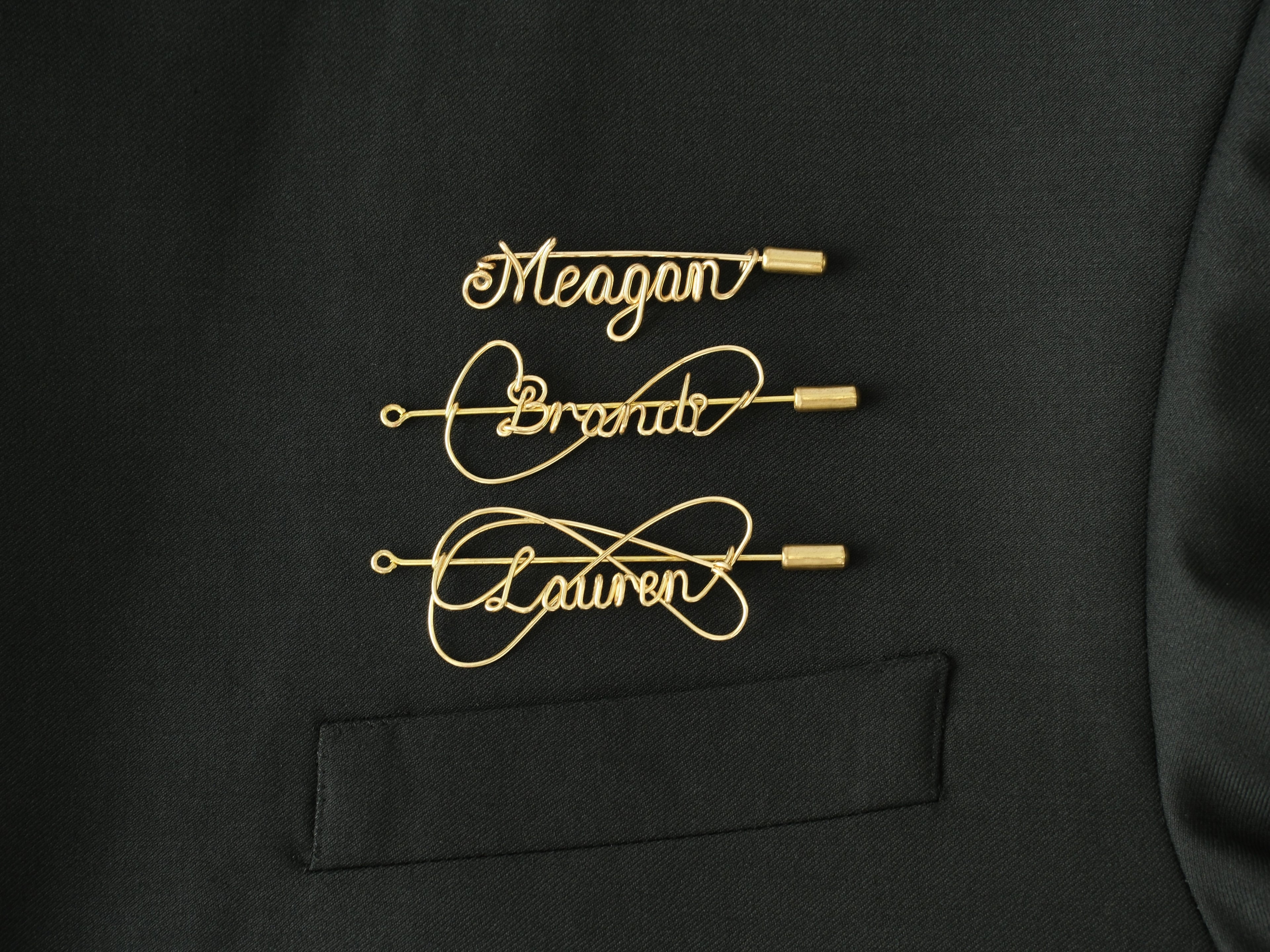 Custom name brooch in gold-plated copper wire on a black jacket, handcrafted jewelry.
