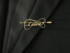 Custom name brooch with elegant double-line intertwined design, in gold-plated copper on a black jacket.