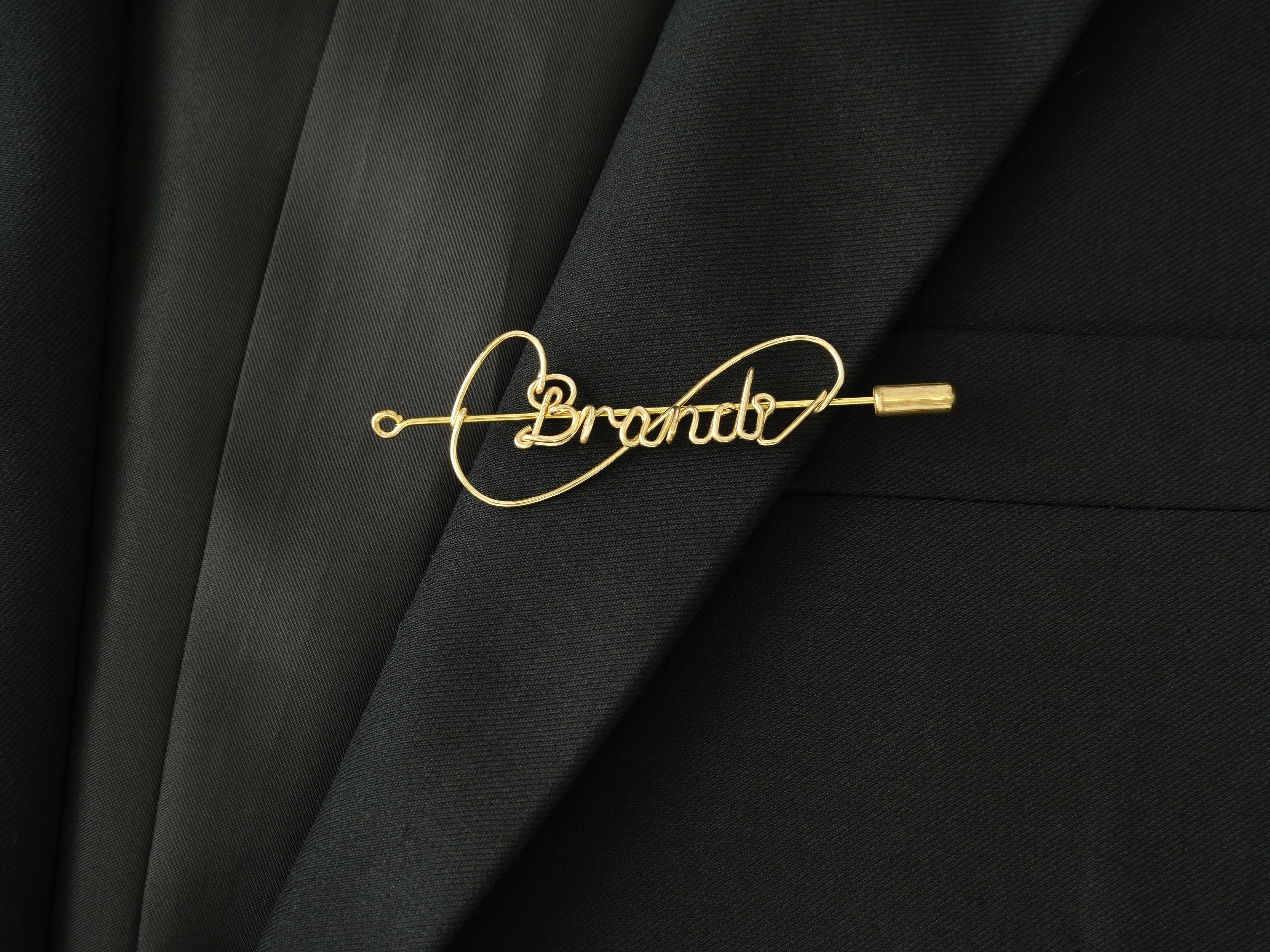 Custom name brooch with modern infinity line design, in gold-plated copper on a jacket lapel.
