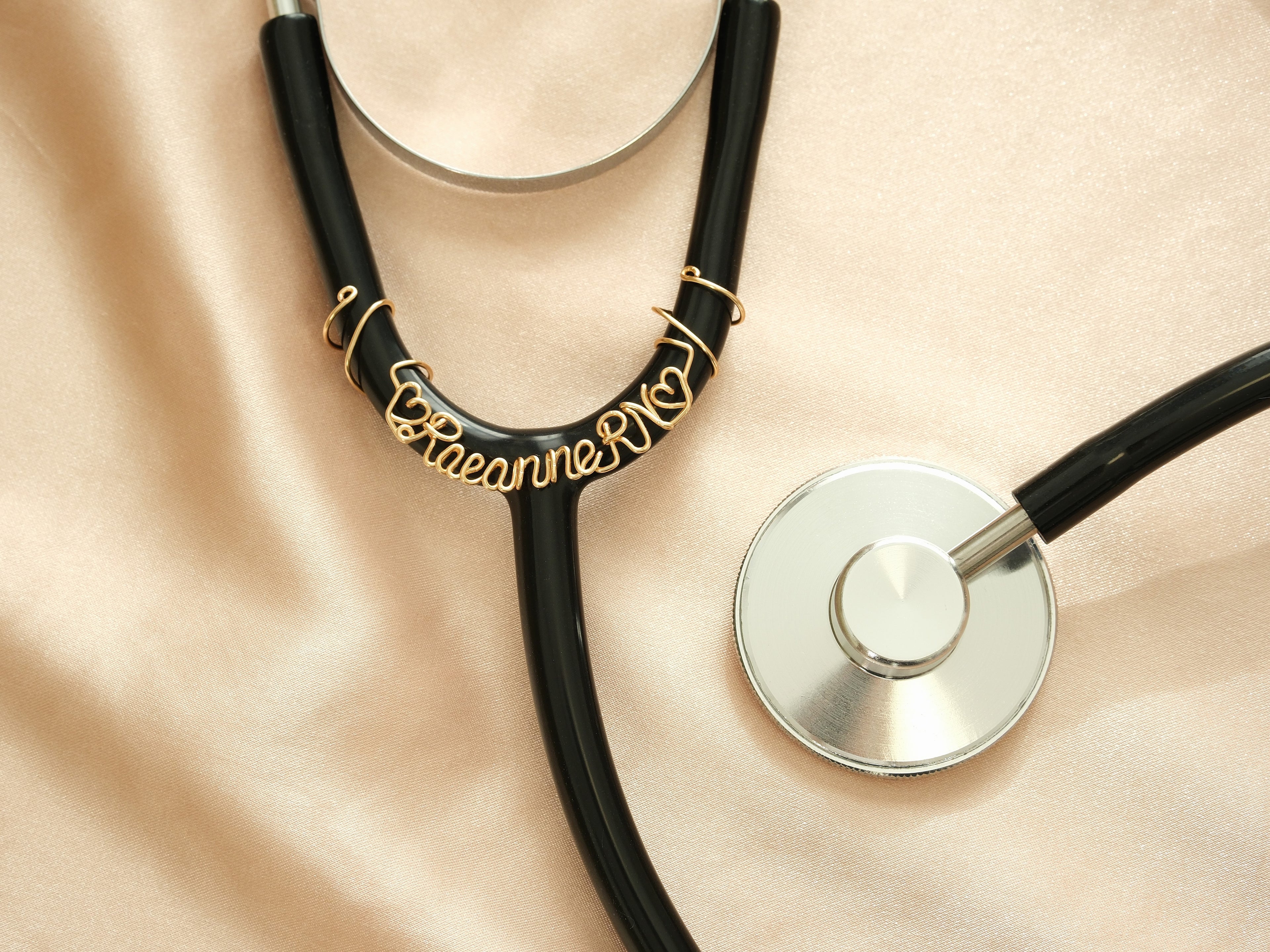 Close-up of a personalized gold stethoscope tag with name and heart symbols, a special gift for Registered Nurses (RN).