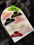 Personalized hair claw clips in vibrant colors on a dark glittery background, featuring a sparkling effect.