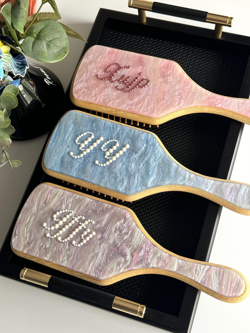 Pink, blue, and purple marble paddle brushes with custom rhinestone names.
