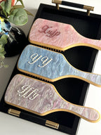 Pink, blue, and purple marble paddle brushes with custom rhinestone names.
