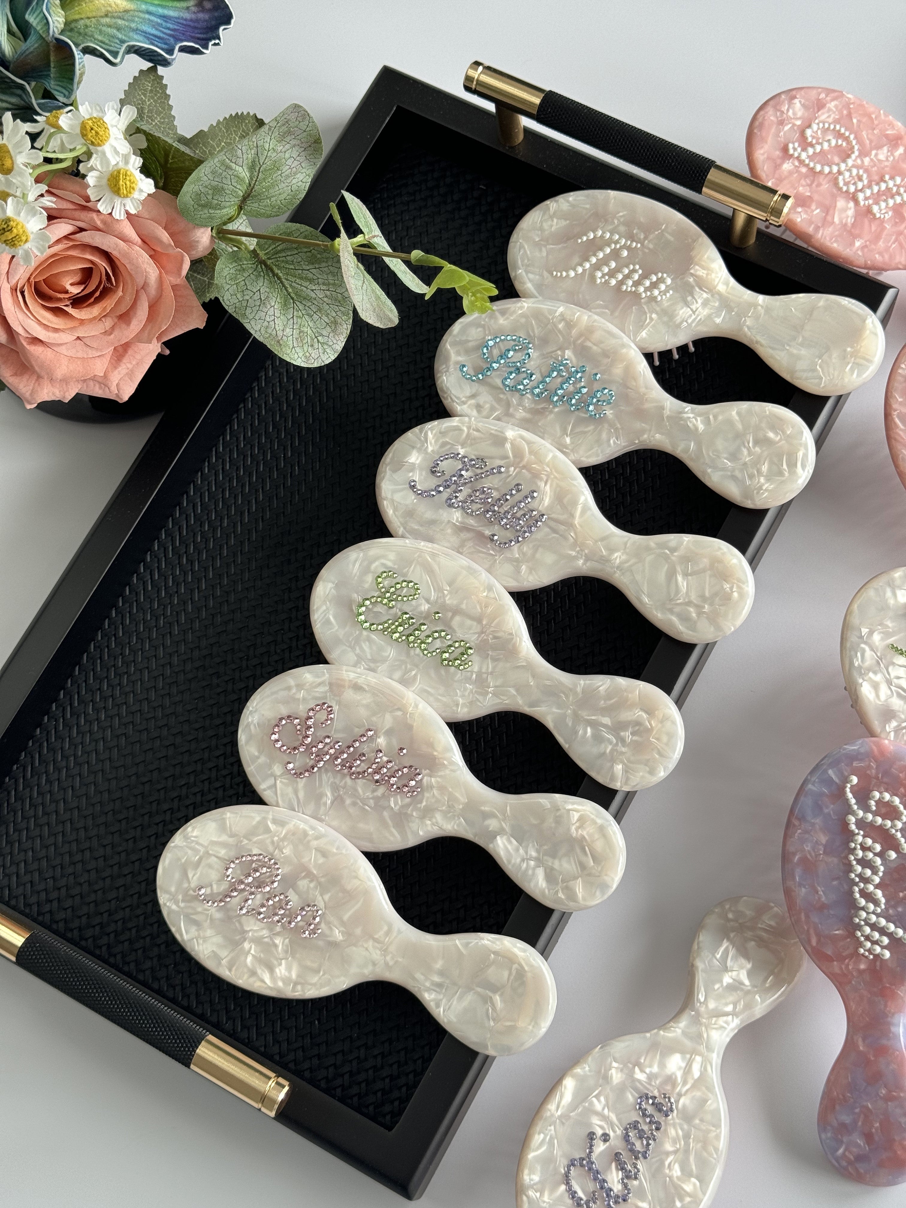 Personalized pearl-white marble mini hair brushes with colorful rhinestone names, a great gift idea for bridesmaids.