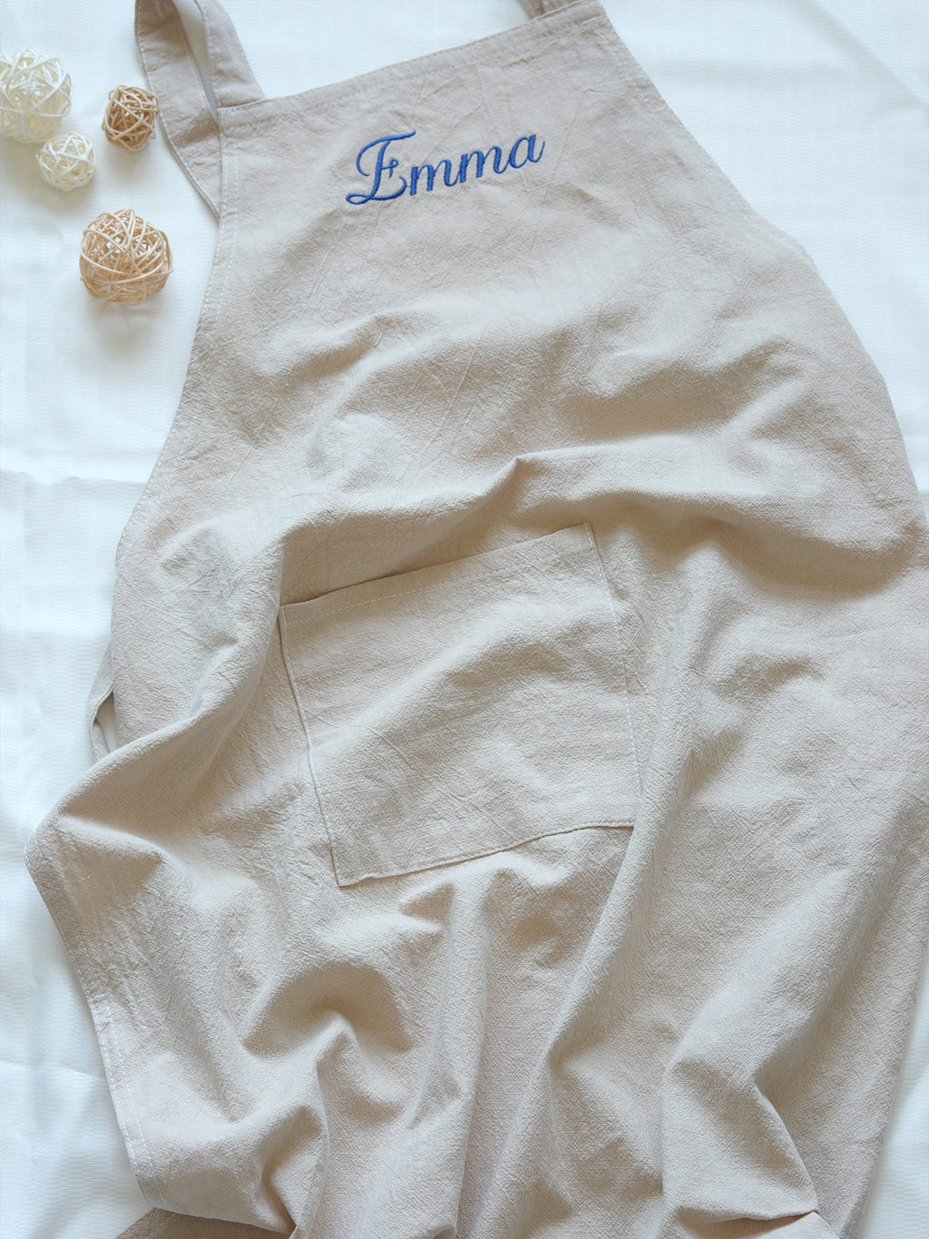 Oat Beige linen apron featuring a large front pocket and "Emma" personalized in blue embroidery.