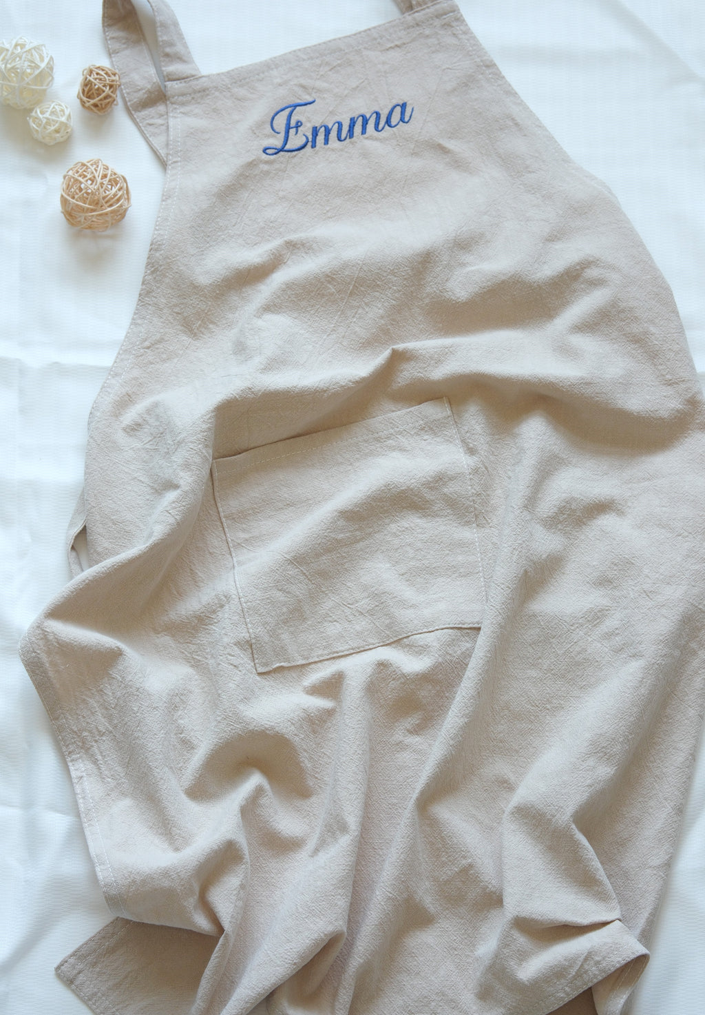 Oat Beige linen apron featuring a large front pocket and "Emma" personalized in blue embroidery.