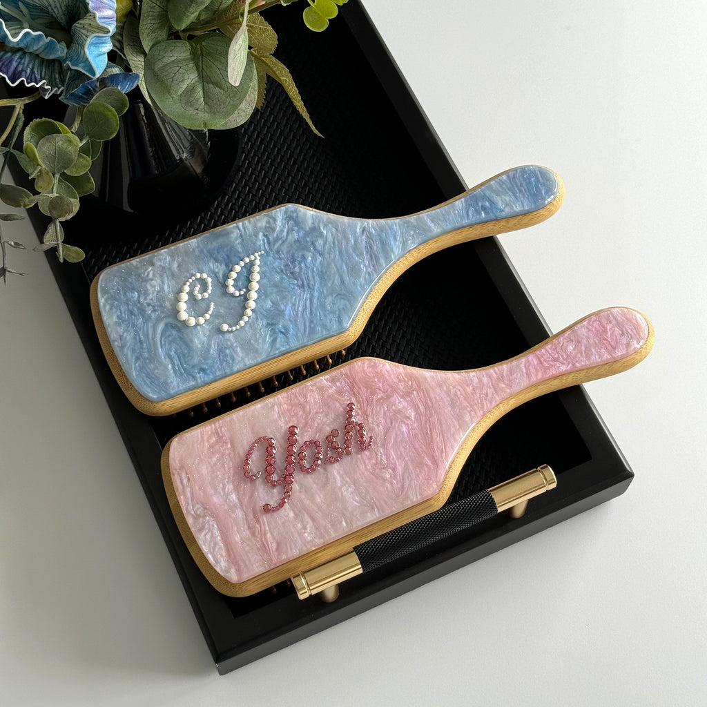 Personalized blue and pink marble paddle brushes with rhinestone names, a perfect gift set for friends.