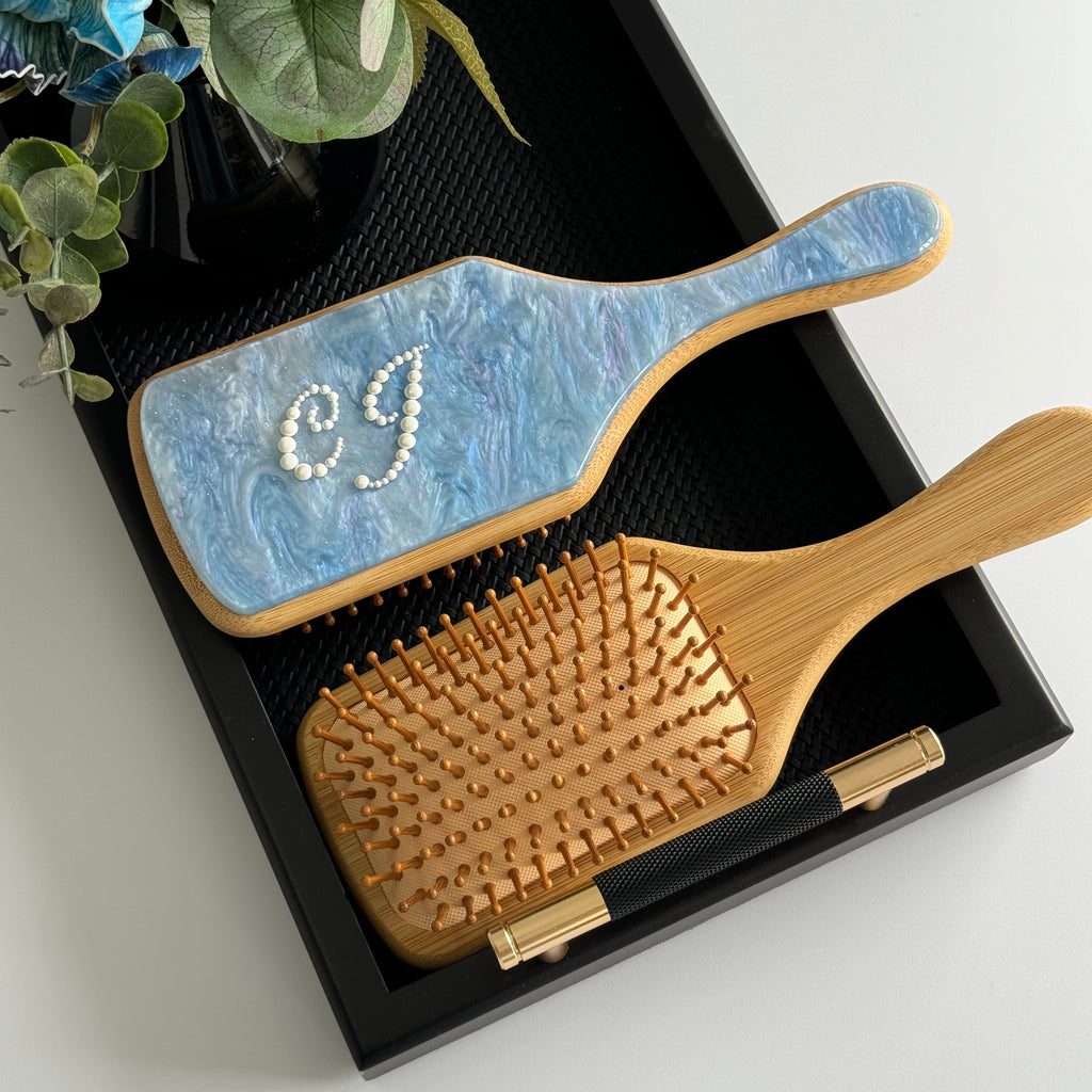Front and back view of the paddle brush: personalized marble finish and wood-effect bristle side.