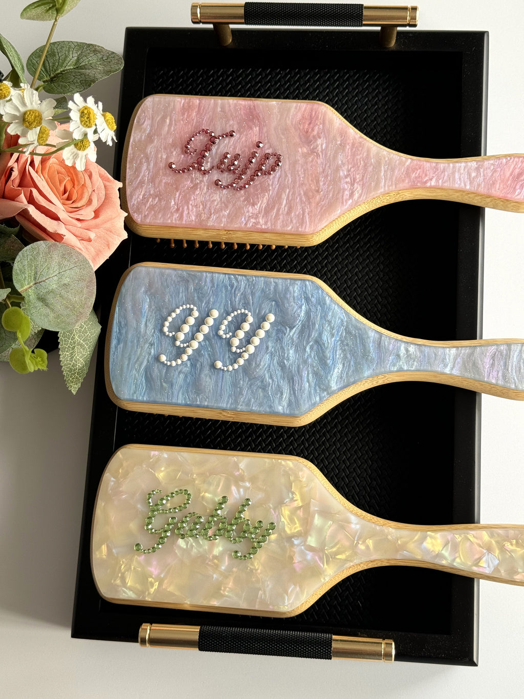 Trio of paddle brushes in pink, blue, and cream marble with personalized rhinestone names.