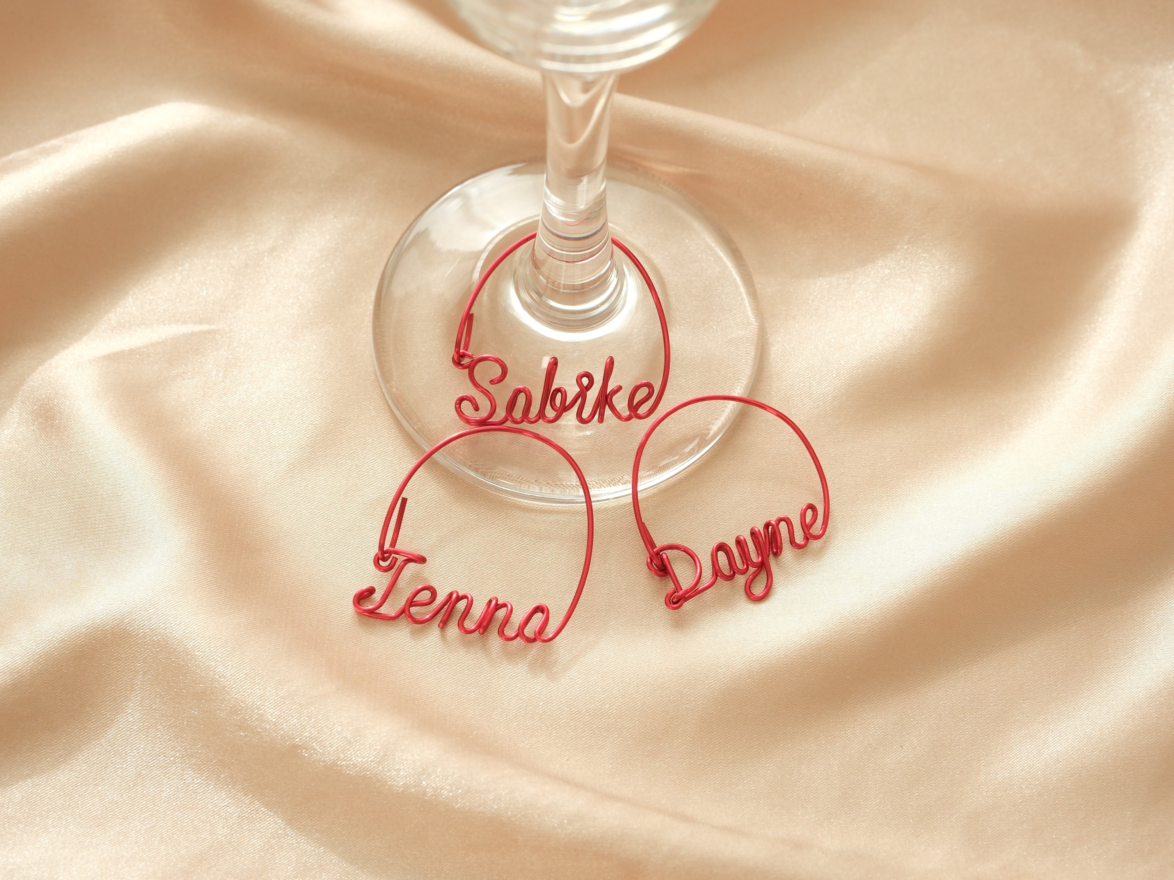 Three personalized red metal wine glass charms with names, elegant decoration for wine glasses and wedding tables.