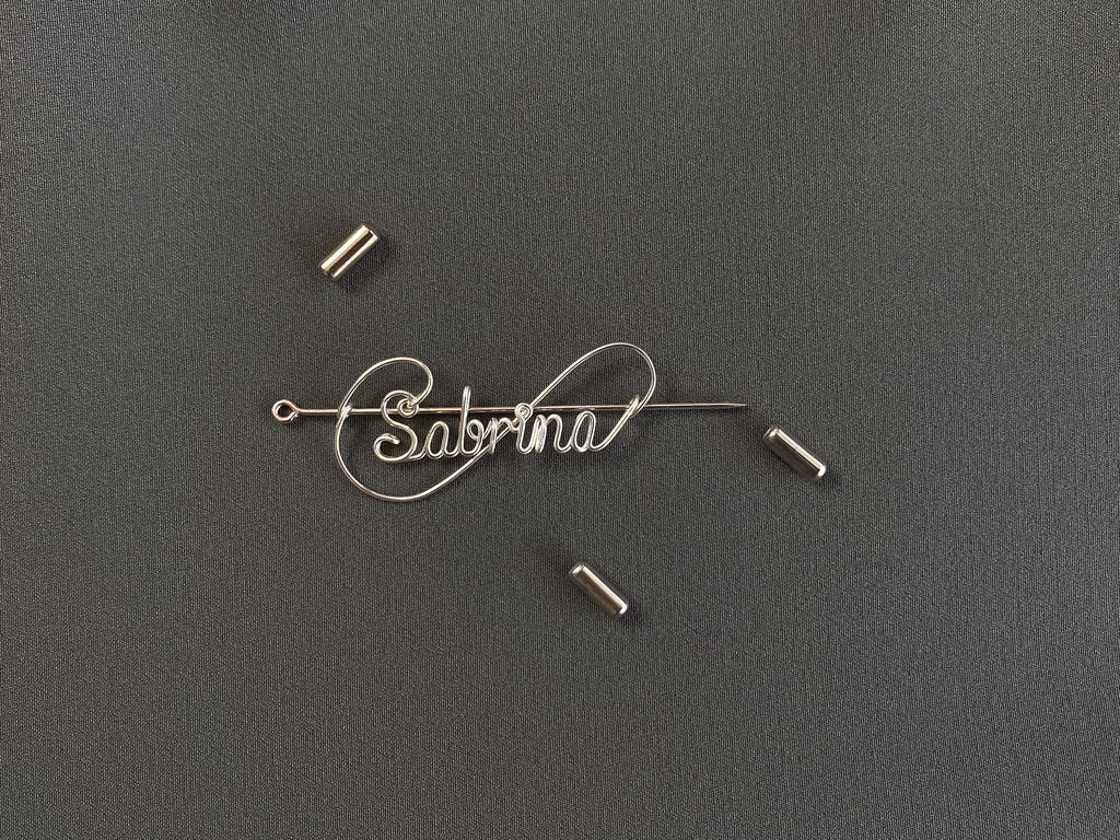 Detailed view of the protective cap closure on a silver-plated name pin over a dark green jacket.