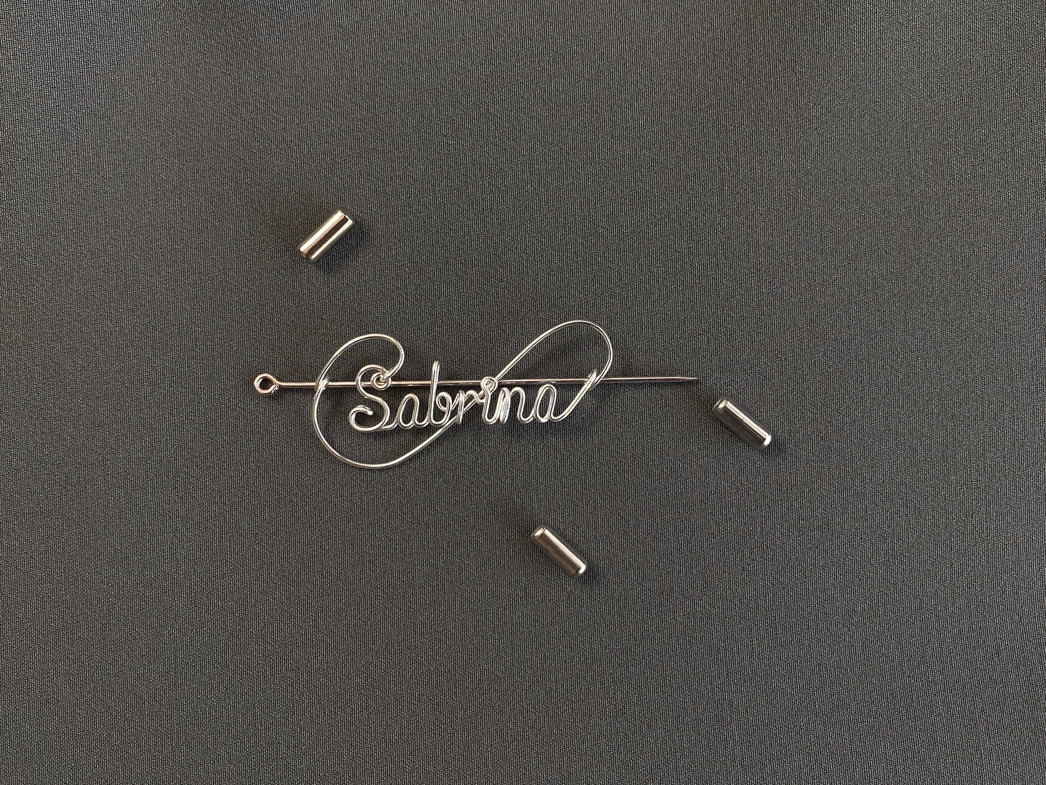 Detailed view of the protective cap closure on a silver-plated name pin over a dark green jacket.