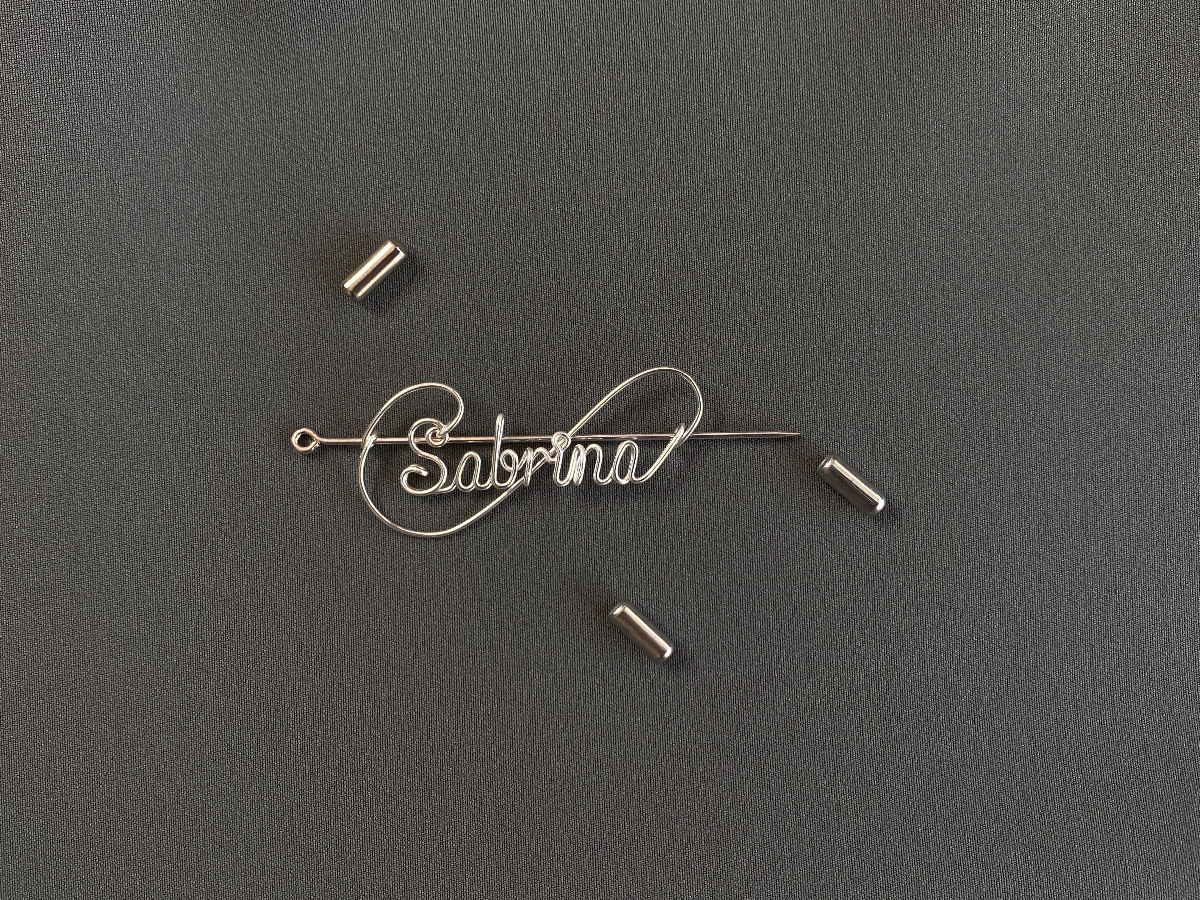 Detailed view of the protective cap closure on a silver-plated name pin over a dark green jacket.