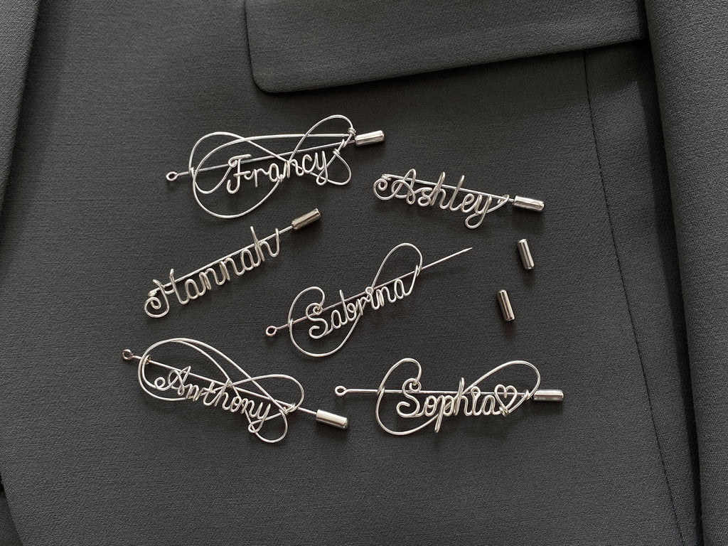 Complete collection of personalized silver-plated name pins in various artistic styles on a dark green jacket.