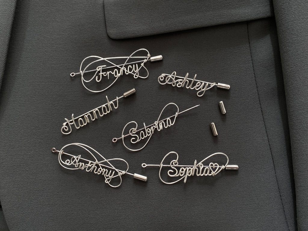 Complete collection of personalized silver-plated name pins in various artistic styles on a dark green jacket.