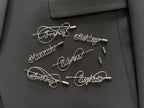Complete collection of personalized silver-plated name pins in various artistic styles on a dark green jacket.