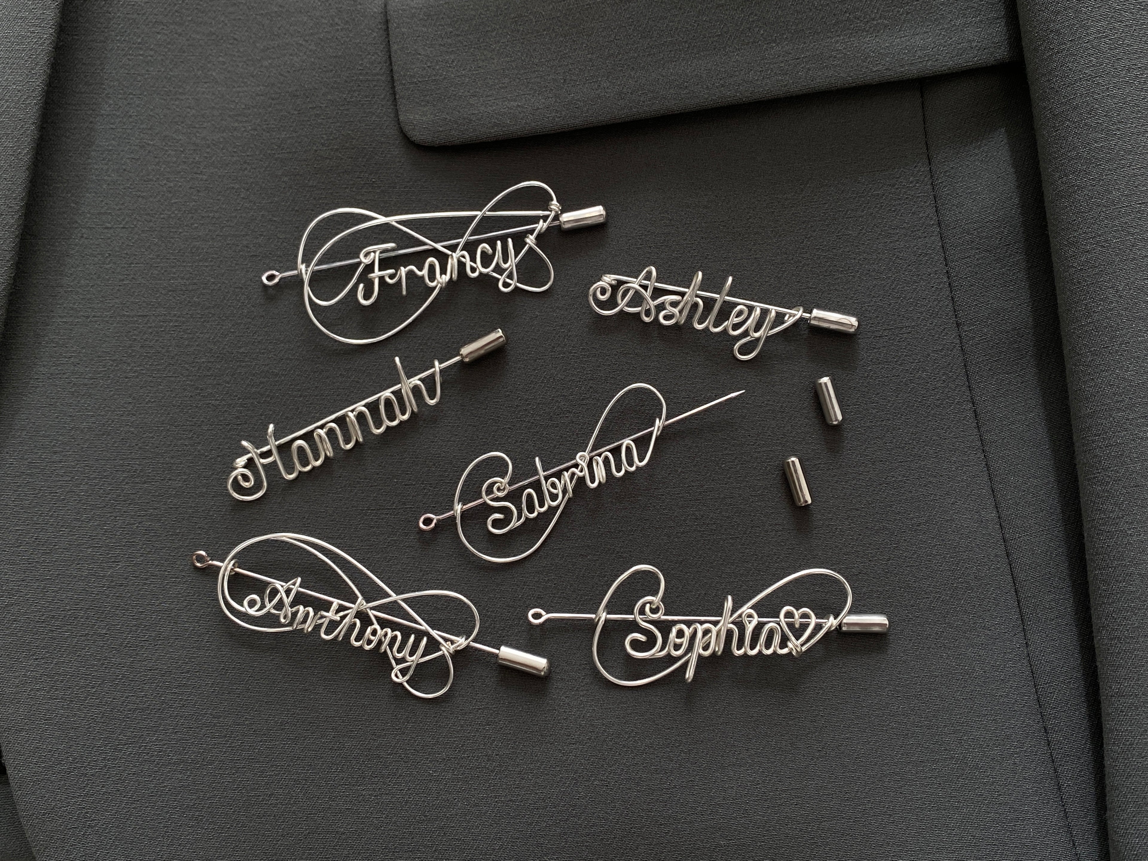 Complete collection of personalized silver-plated name pins in various artistic styles on a dark green jacket.