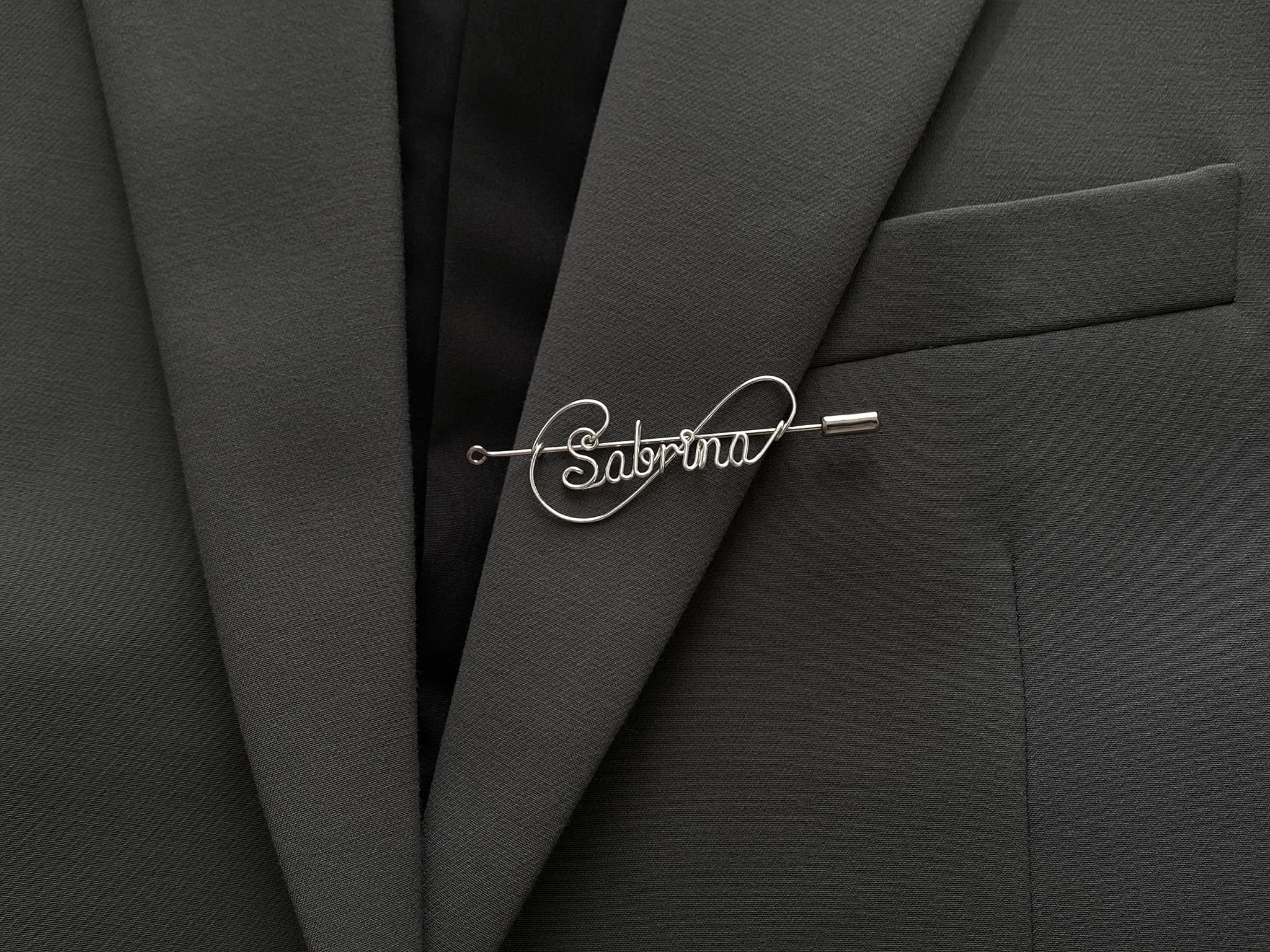 Modern infinite-line design personalized name pin, crafted in silver-plated finish on a dark green jacket.