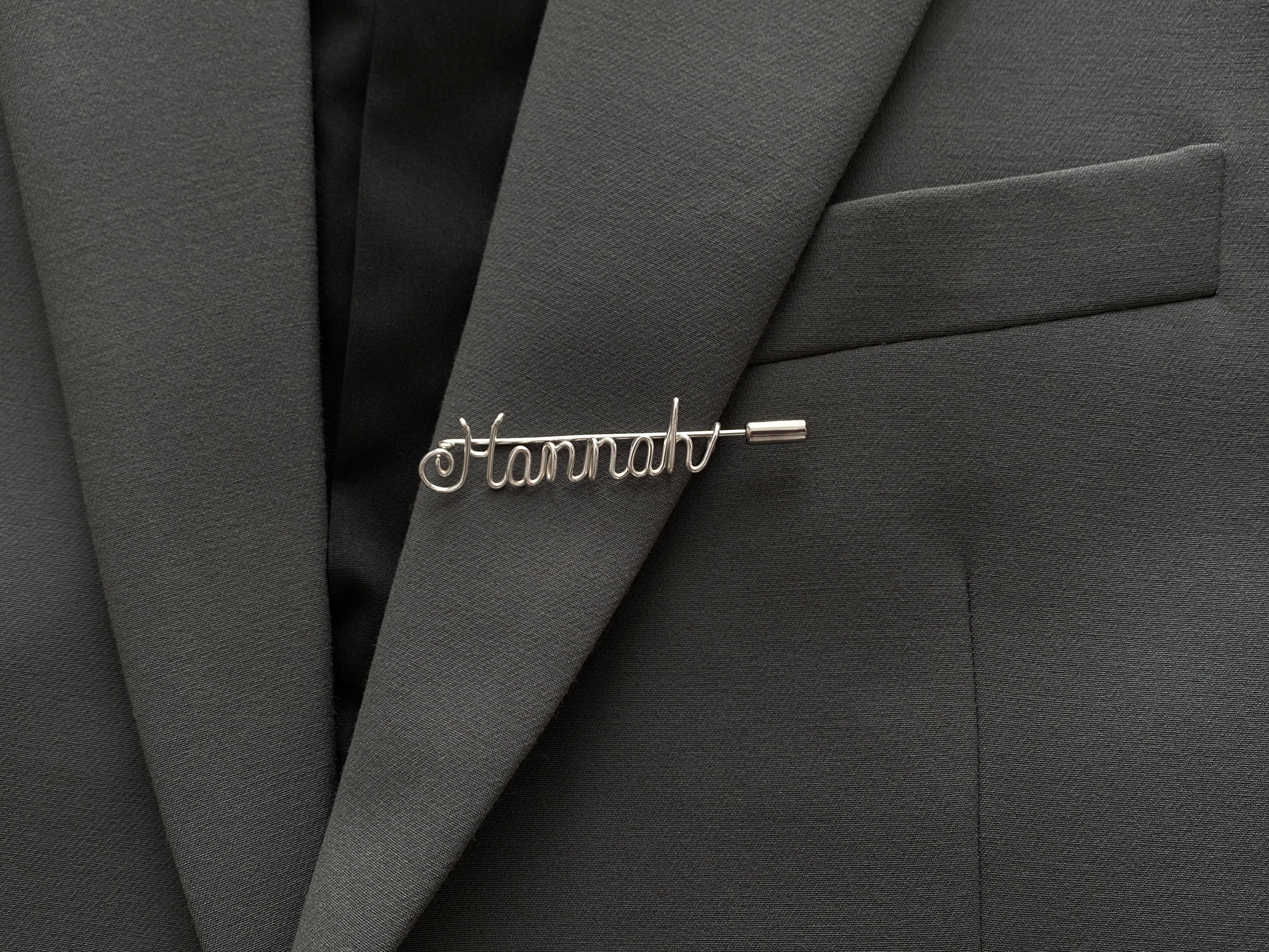 Minimalist personalized name pin, handmade in silver-plated finish on a dark green jacket.