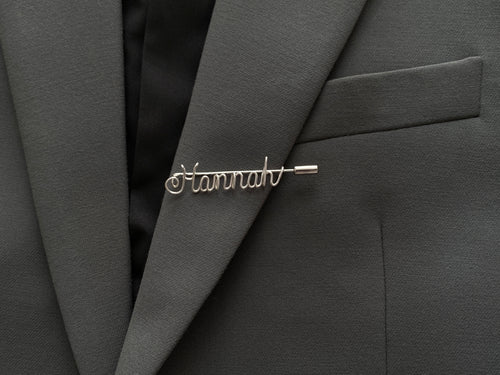 Minimalist personalized name pin, handmade in silver-plated finish on a dark green jacket.