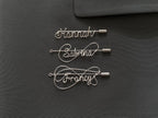 Three styles of personalized silver-plated name pins on a dark green jacket, handcrafted design.