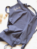 Slate Blue linen apron personalized with "Sydney" embroidery and a spacious central pocket.