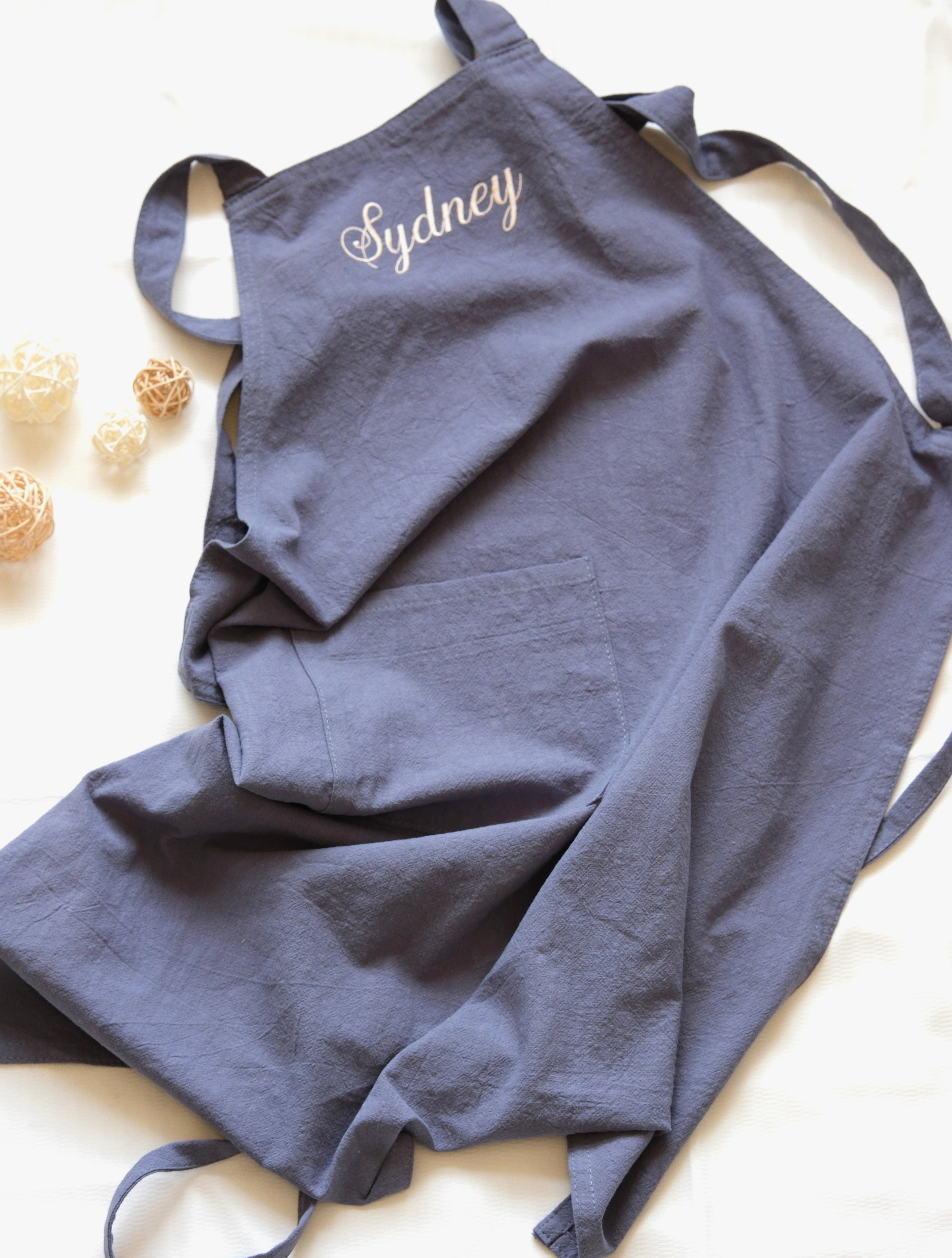 Slate Blue linen apron personalized with "Sydney" embroidery and a spacious central pocket.