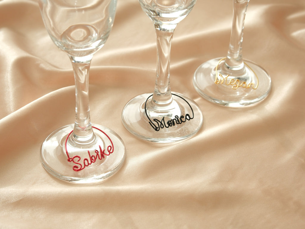 Personalized wine glass charms in red, black, and gold metal, perfect for distinguishing guests' drinks.